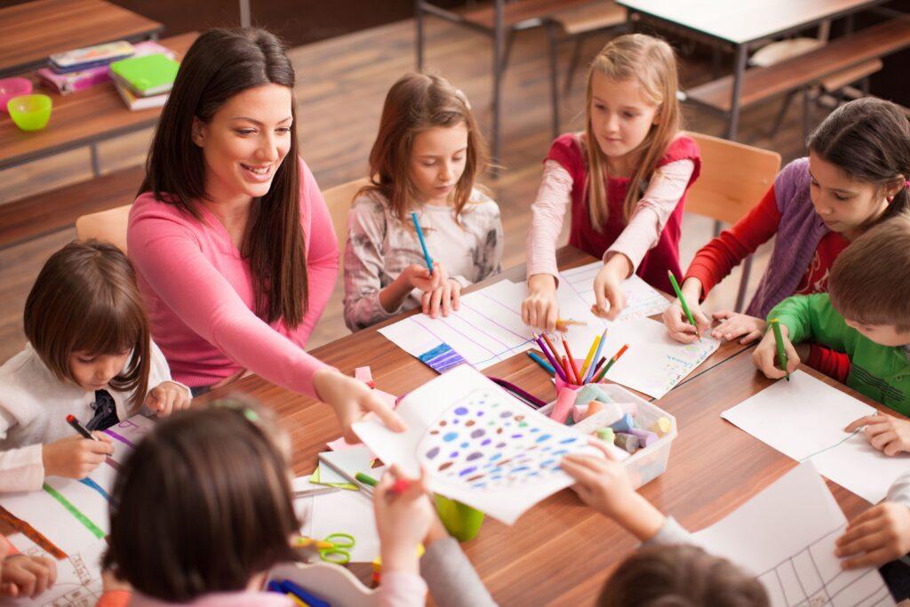 Erzieherin mit Kindern malen Bilder an einem Tisch