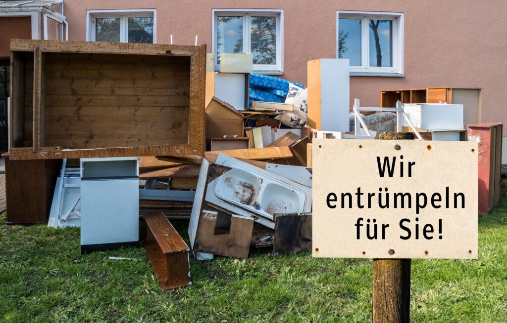 Ein Schild auf dem "wir entrümpeln für sie" steht, dahinter liegt Sperrmüll