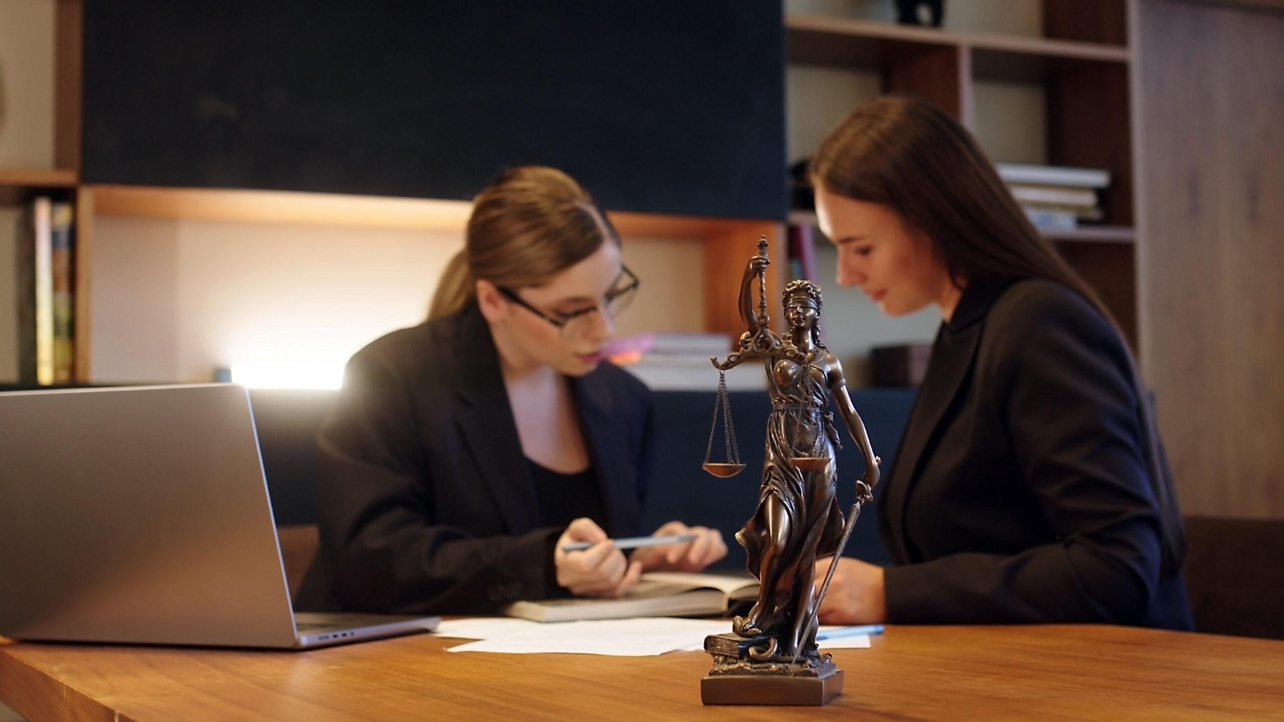 Zwei Anwältinnen bei einer Besprechung mit einer Justitia-Statue im Vordergrund – kompetente Rechtsberatung durch Rechtsanwälte Mönchengladbach.