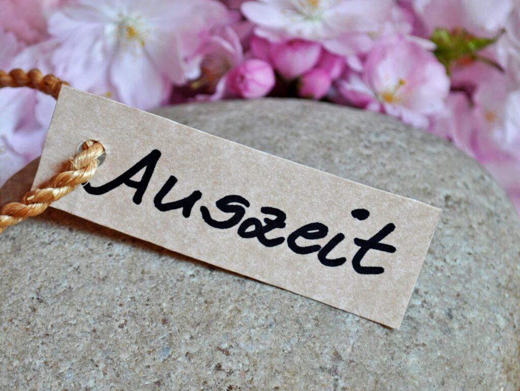 Schild mit „Auszeit“ auf Stein mit Blüten.