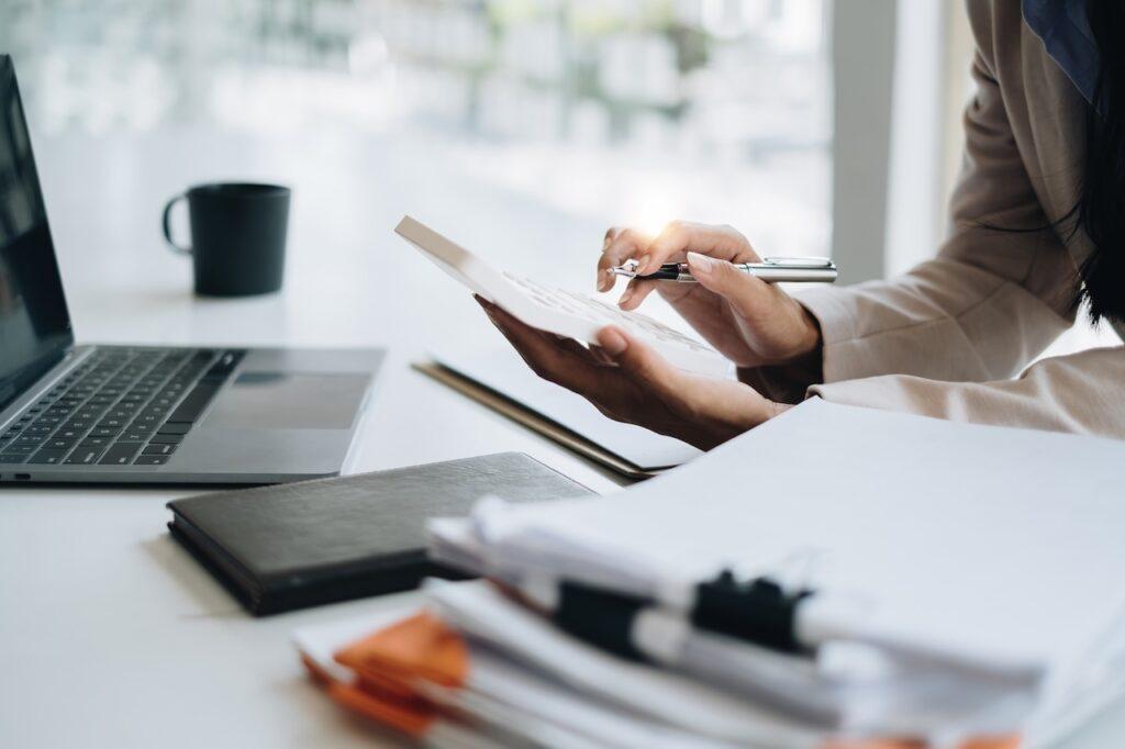 Frau arbeitet mit Taschenrechner und Dokumenten am Laptop – optimierte Lohnabrechnung durch Outsourcing.