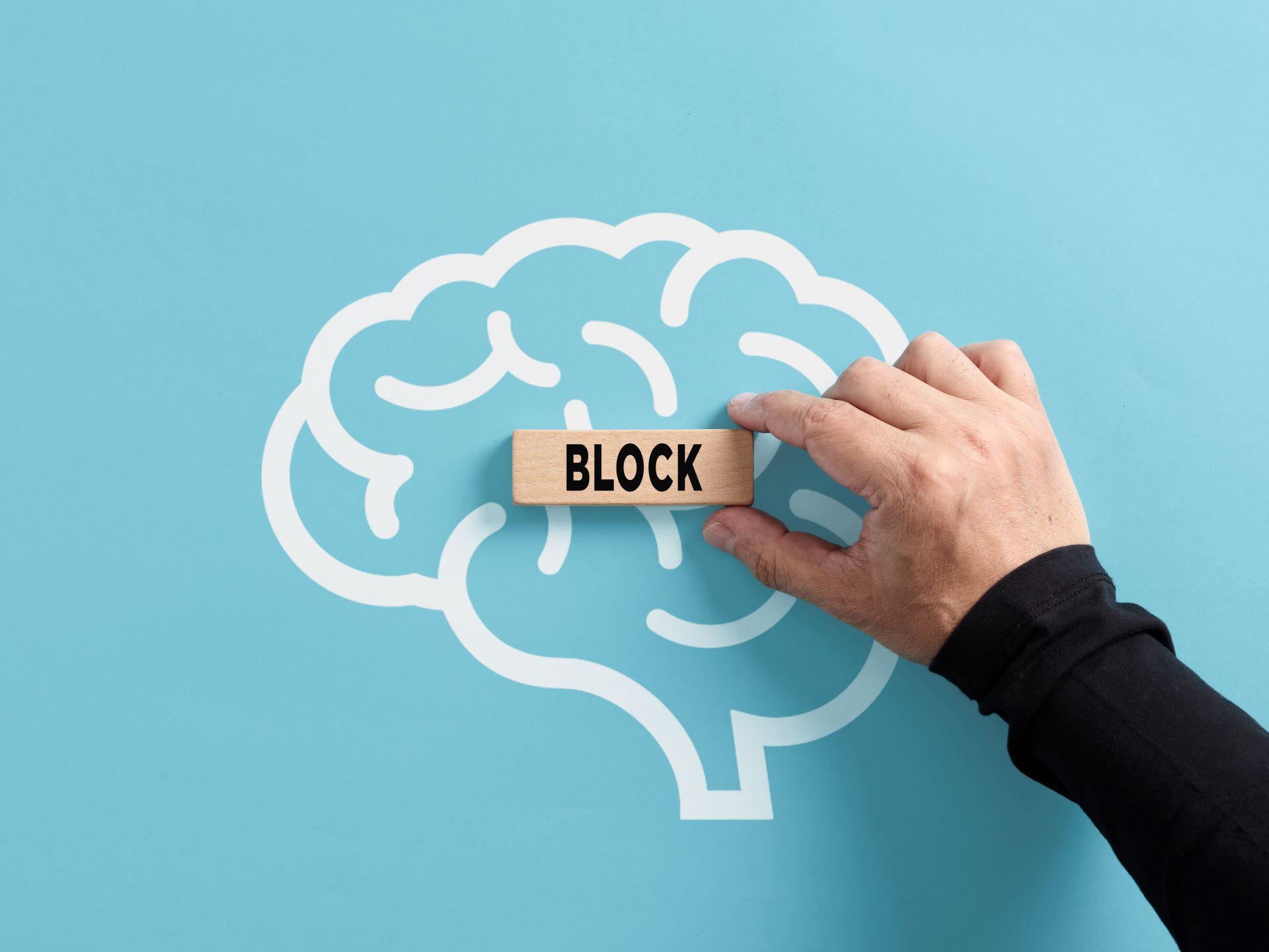 Holzblock mit „BLOCK“ vor grafischem Gehirn als Symbol für mentale Blockaden