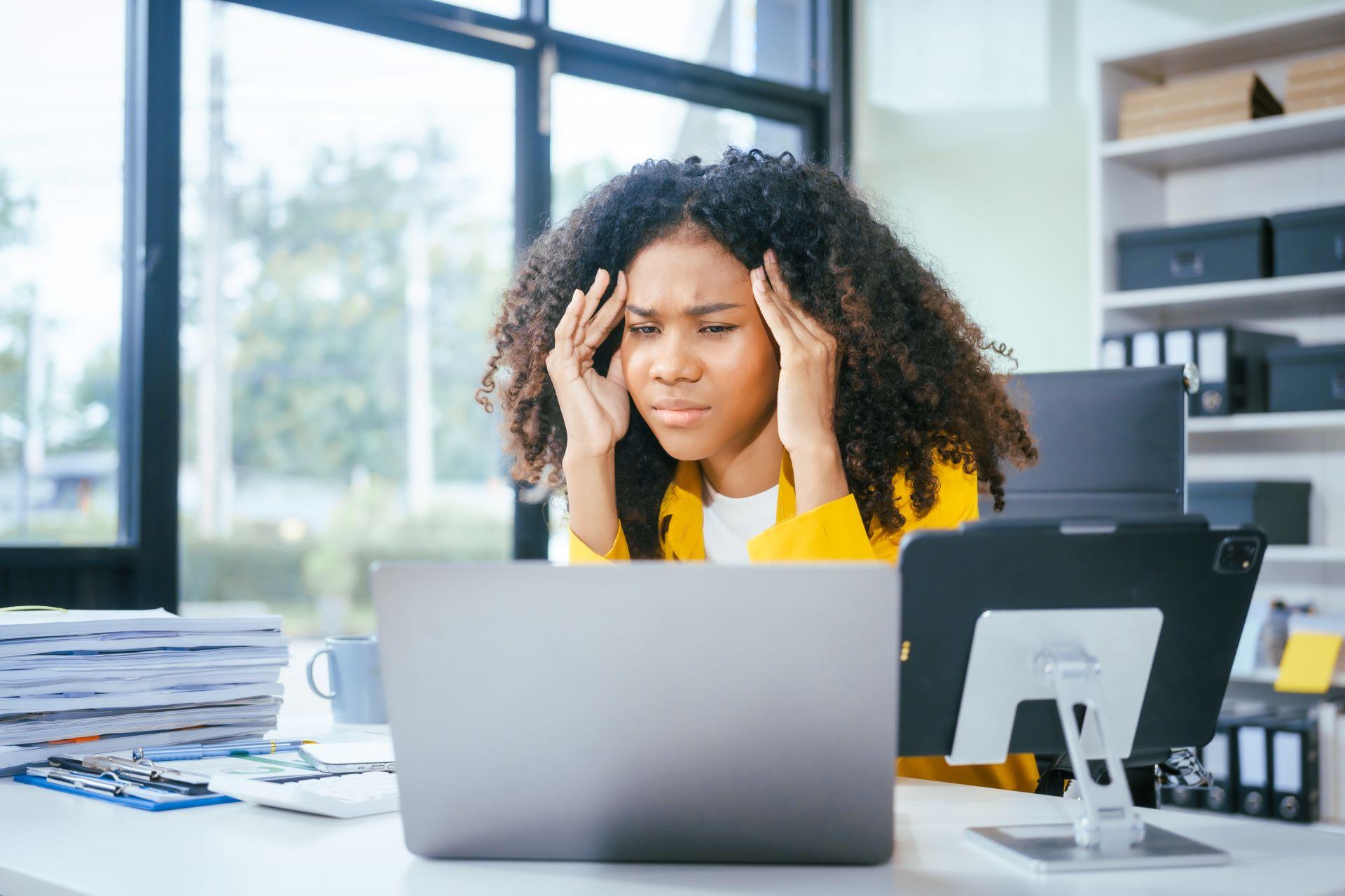 Gestresste Frau im Büro mit Händen an der Stirn vor Laptop